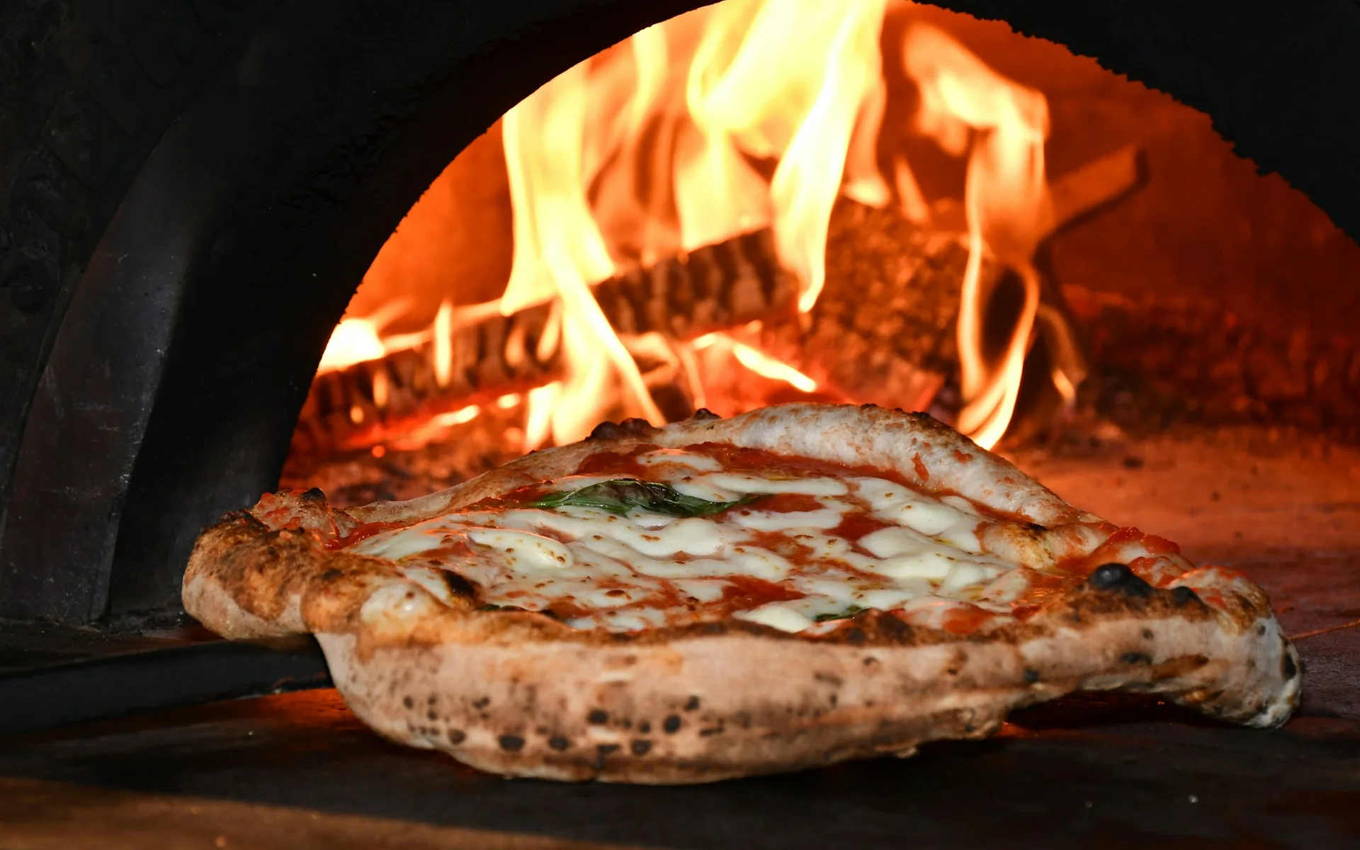 A pizza baking beside the flames